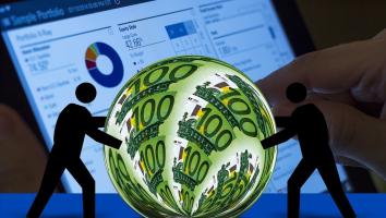 Silhouetted figures appear to push a sphere covered in 100 Euro notes. Behind them, a financial dashboard with graphs and data is visible on a screen, suggesting a concept of global finance and market analysis.