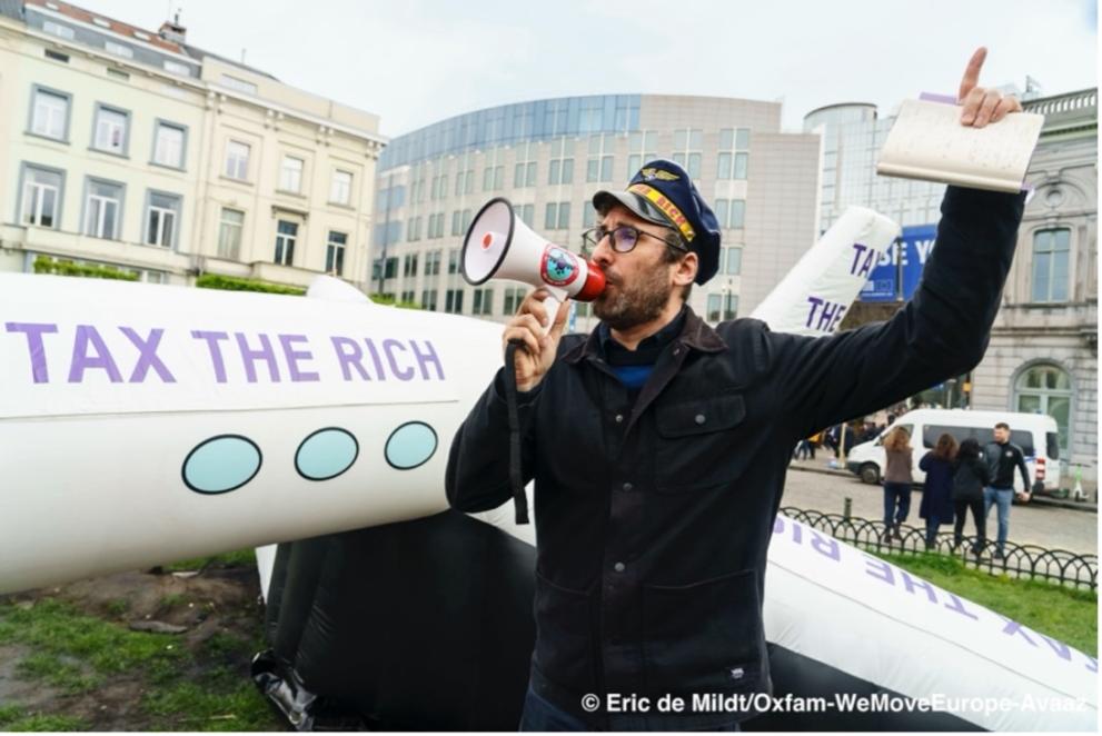 Blow up airplane with "tax the rich" on the side next to a man wearing a pilot outfit and hat