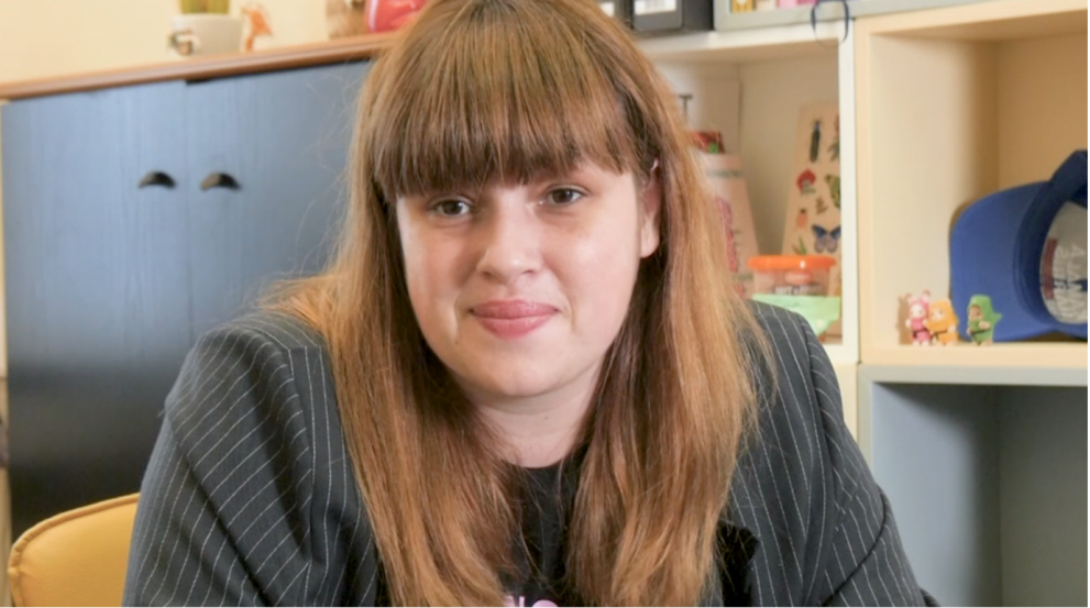woman with long light brown hair with bangs wearing a pinstripe grey blazer