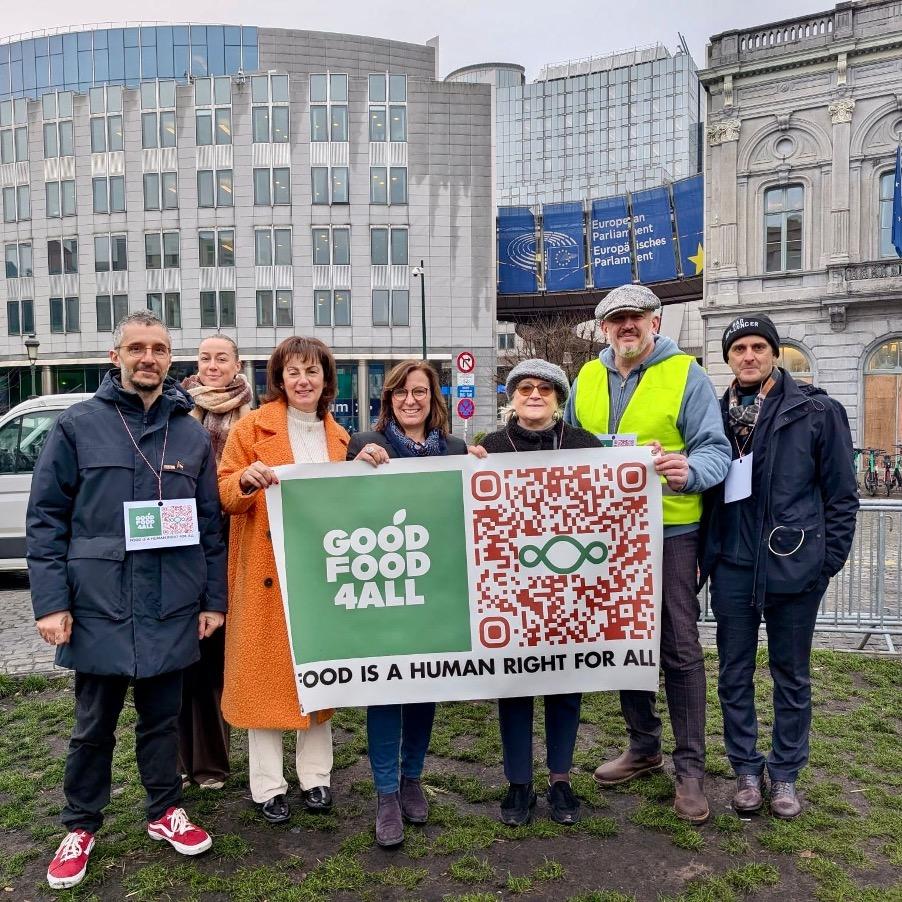 Eight people stand together outside the European Parliament holding a “Good Food 4 All” banner with the message “Food is a human right for all” and a large QR code.