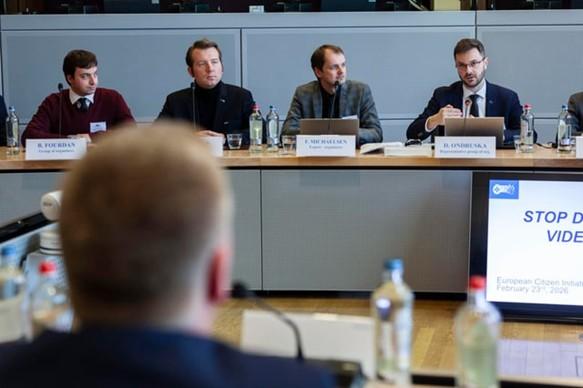 A panel of 4 speakers sits behind a long desk in a conference room, facing an audience. They are speaking into microphones and looking at documents or screens. These people are the Organisers of Stop Destroying Videogames ECI during the meeting at the European Commission