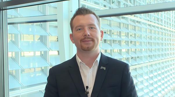 Pavel Zálešák, member of the group of organisers of Stop Destroying Videogames in a suit stands indoors in front of a large glass window, facing the camera with a slight smile during ECI Day.